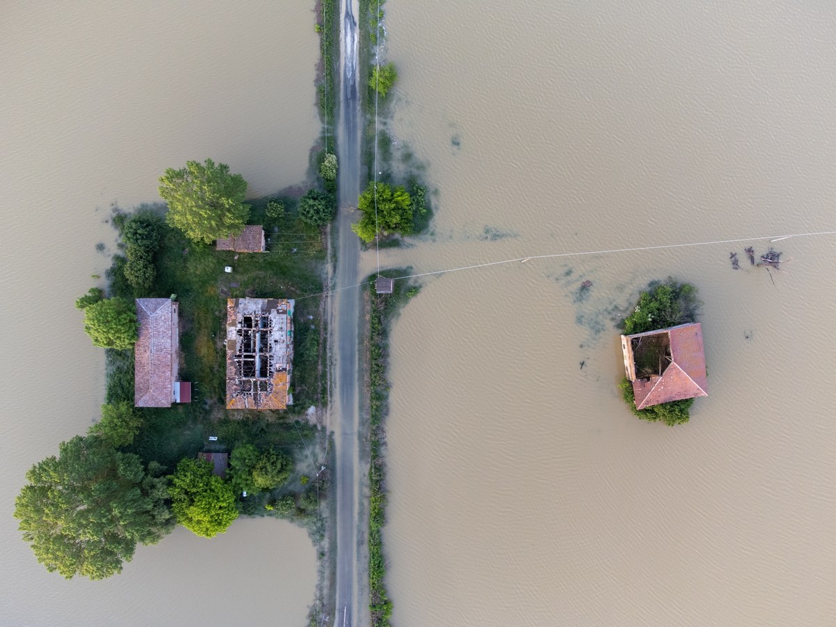 Campagna allagata da un’alluvione, con acqua torbida che ricopre i campi; piccolo nucleo di case con i tetti devastati. Campagna allagata da un’alluvione, con acqua torbida che ricopre i campi; piccolo nucleo di case con i tetti devastati.
