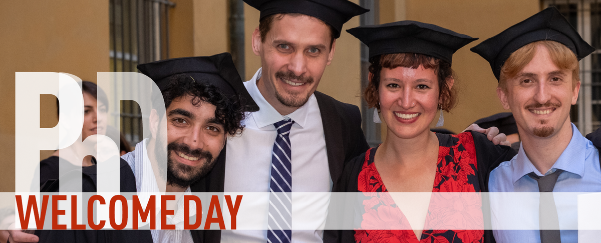 PhD Welcome Day. Una dottoranda con toga a tocco sorride nel giorno dell'addottoramento in mezzo ad altre e altri dottorande